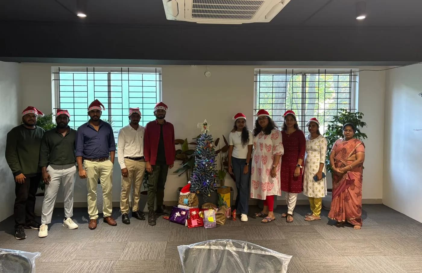 Team members in Santa hats beside a Christmas tree in the office